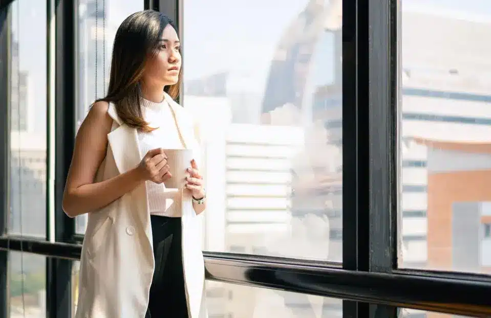 Woman holding mug staring at window at cityscape